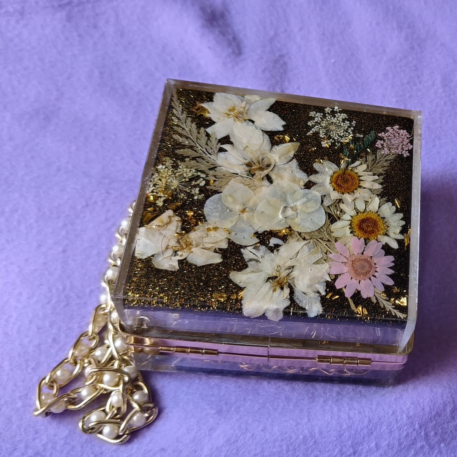 Small decorative box with pressed flowers and a chain on a purple background
