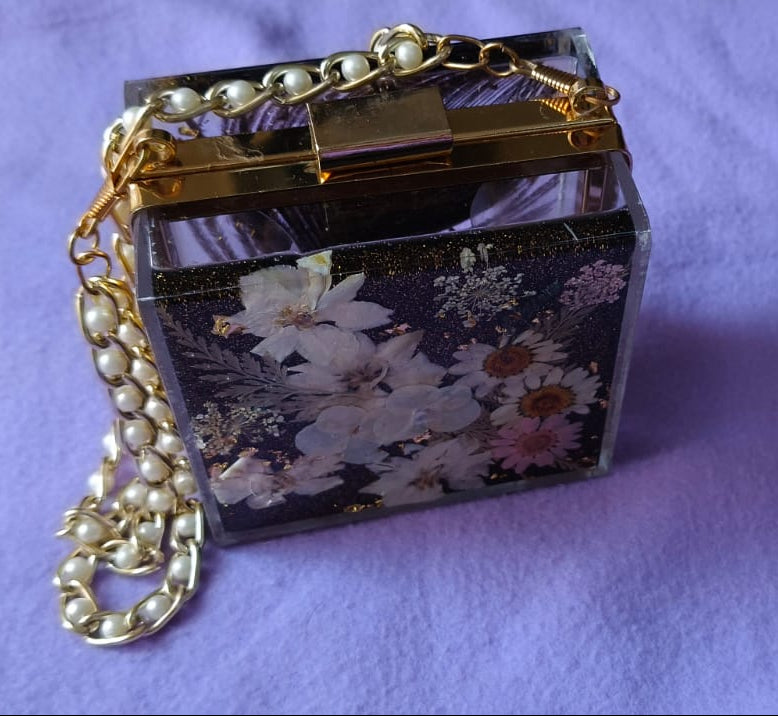 Small decorative box with floral pattern and gold chain on a purple fabric background