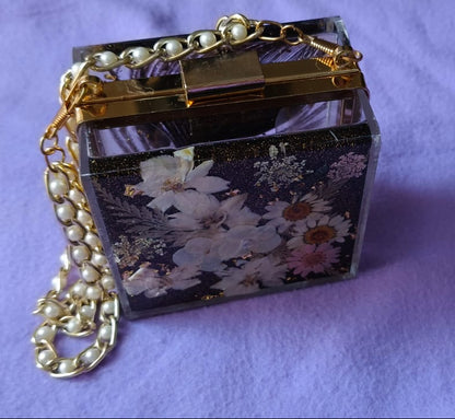 Small decorative box with floral pattern and gold chain on a purple fabric background