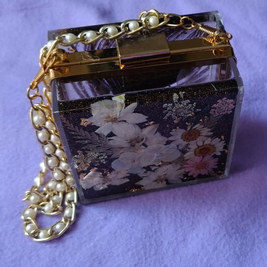 Small decorative box with floral design and pearl chain on a purple background