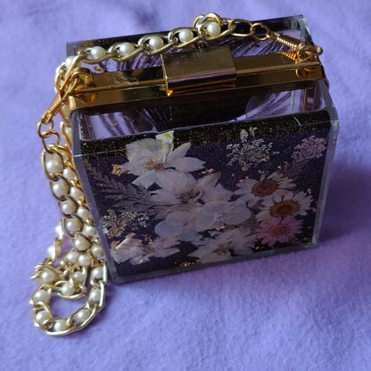 Small decorative box with floral design and pearl chain on a purple background