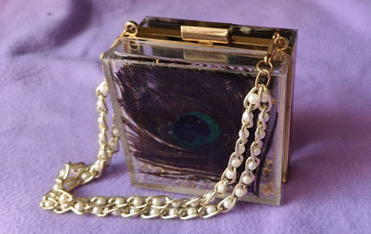 Clear handbag with gold chain strap on a purple background